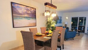 A dining area with a wooden table and wicker chairs, a fruit bowl, and a hanging light fixture. - Island life 2 br 2-ba walk 2 beach, Snorkel & Surf (West Palm Beach)