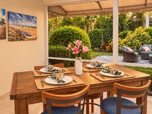 Een houten eettafel gedekt met placemats, borden en bestek, omringd door stoelen, met een bloevas in het midden.