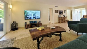 A living room with a large TV, a wooden coffee table, a green sofa, and a decorative birdcage. - Island life 2 br 2-ba walk 2 beach, Snorkel & Surf (West Palm Beach)