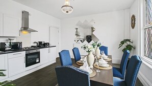 Una cucina moderna con mobili bianchi, una cappa aspirante in acciaio inossidabile e un'area pranzo con sedie imbottite blu e un tavolo in legno apparecchiato per quattro persone.