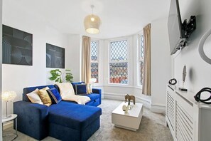 A modern living room with a blue sofa, a white coffee table, and a large window with curtains. - Home in Woodhouse, Leeds | Free Parking|Free WiFi (Woodhouse)