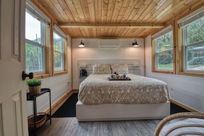 A bedroom with a wooden ceiling, large windows, a bed with a tray of items, and a fan. - Cozy cabin in charming Cosby with AC (Cosby)
