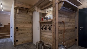 A rustic interior with wooden walls, a fireplace with antlers, a fur stool, and a metal bucket.