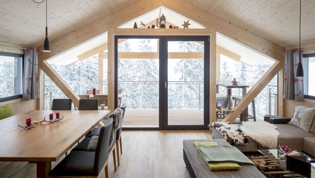 A cozy cabin with a wooden interior, a dining area, and a seating area with a view of snow-covered trees.