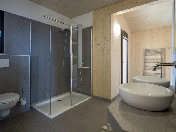 Et moderne badeværelse med et glasafskærmet brusebad, et toilet og to store håndvaske.