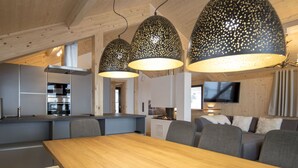 Eine moderne Küche mit eingebauten Geräten, ein Essbereich mit einem Holztisch und grau gepolsterten Stühlen und eine gemütliche Sitzecke mit Kamin.