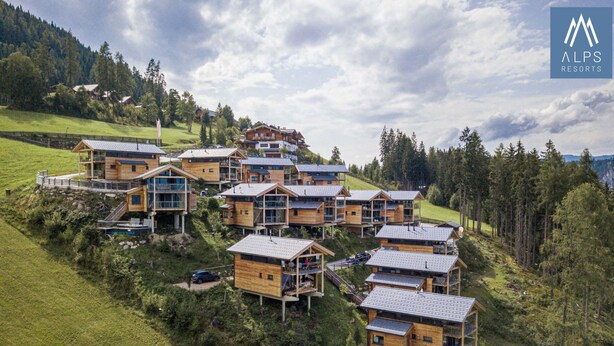 Un ensemble de chalets en bois dotés de balcons, situés sur une colline et surplombant une forêt.