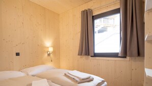 Une chambre avec deux lits, des murs en bois, une fenêtre avec des rideaux et un luminaire fixé au mur.