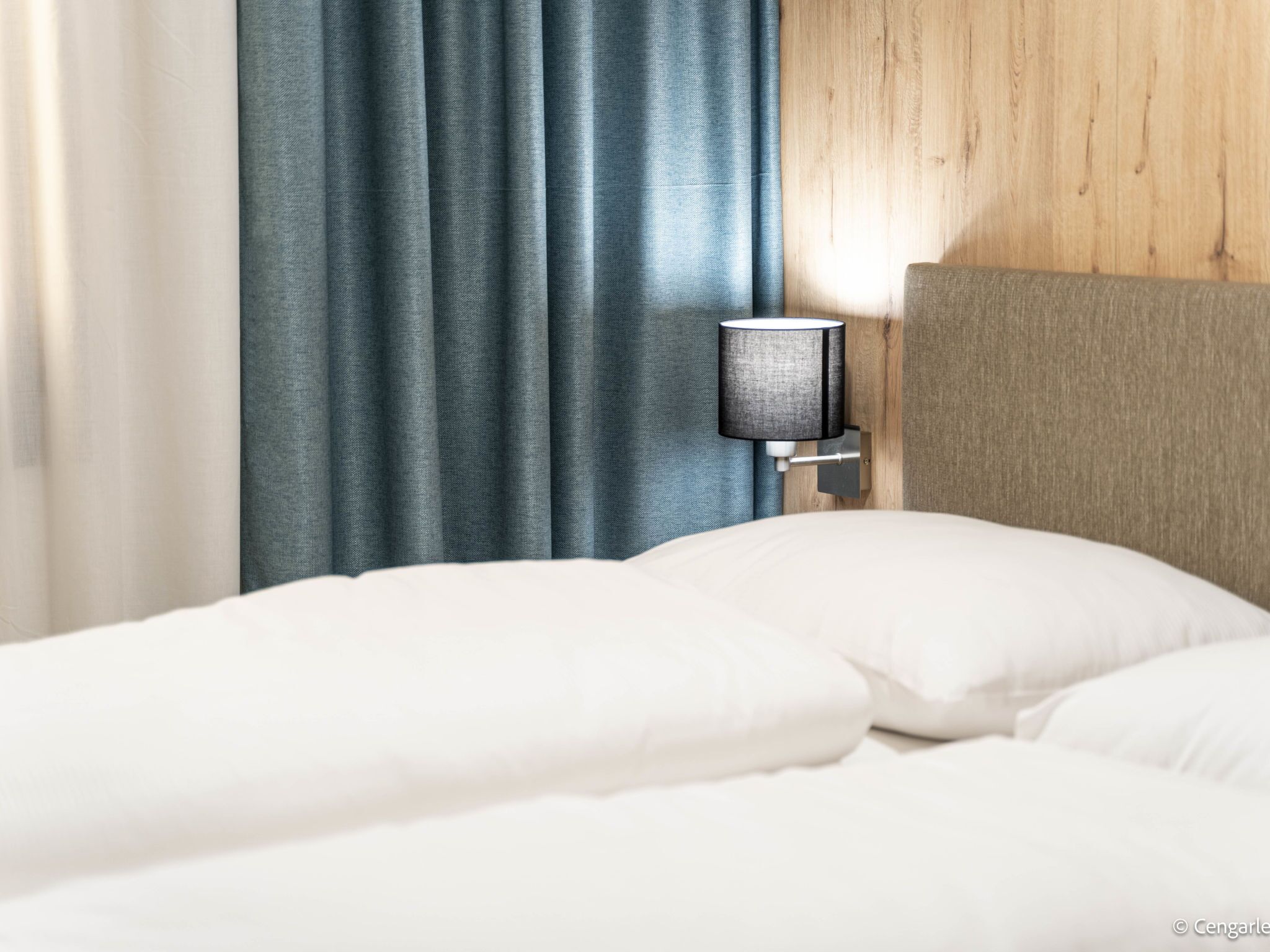 A neatly made bed with white linens, a wall-mounted lamp, and a wooden headboard.