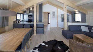 Un loft spacieux avec un plafond haut, des poutres apparentes, un coin cuisine, une table à manger, un canapé et un tapis en peau de vache.