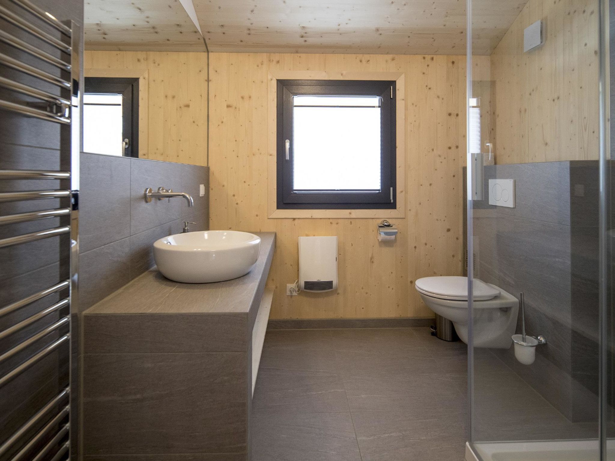 A modern bathroom with a wooden wall, a large window, a sink, and a toilet.