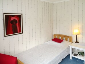 Habitació amb un llit individual, panell frontal de fusta, tauleta de nit amb una làmpada i una almoçada vermella.