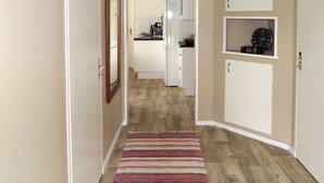 Un corridoio che conduce a una cucina con mobili bianchi, pavimento in legno e tappeto a righe.