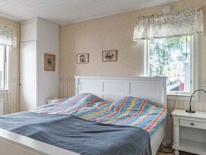 A bedroom with a bed, a nightstand, a window with a floral valance, and two framed pictures on the wall.