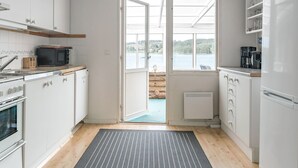 A modern kitchen with white cabinets, a microwave, a stove, and a coffee maker. There is a large window with a view of a lake and trees.
