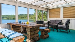 A sunroom with a view of a lake, wooden furniture, and a large window.