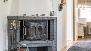 A stone fireplace with a metal door, a brass kettle, and a black rug in a room with wooden flooring and white walls.