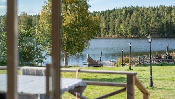 Blick auf einen See mit einer Holzterrasse, einem Pavillon und einem Steg, der ins Wasser hineinreicht.