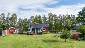 Ein rotes Haus mit Veranda und Garage, umgeben von einem grünen Rasen und Bäumen im Hintergrund.