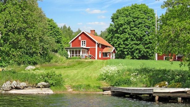Una casa rossa con un portico, circondata da vegetazione e un corpo d'acqua.