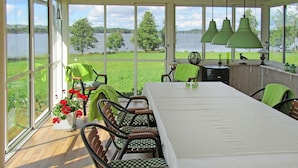 Un'area pranzo coperta con vista su un lago, con un tavolo lungo, sedie e lampade a sospensione.