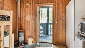 Un intérieur en bois avec une porte donnant sur l’extérieur, un poêle d’époque et un réfrigérateur blanc.