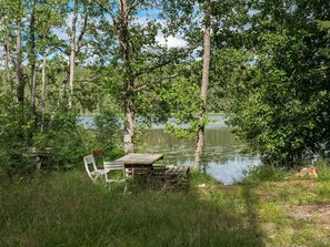 Eine rustikale Holzbank und ein Stuhl am Ufer eines stillen Sees, umgeben von Bäumen.
