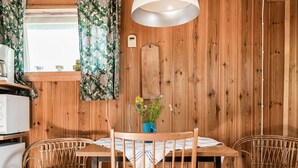 Une pièce aux murs lambrissés, avec une table et deux chaises en osier, un petit vase bleu contenant des fleurs et une lampe blanche.