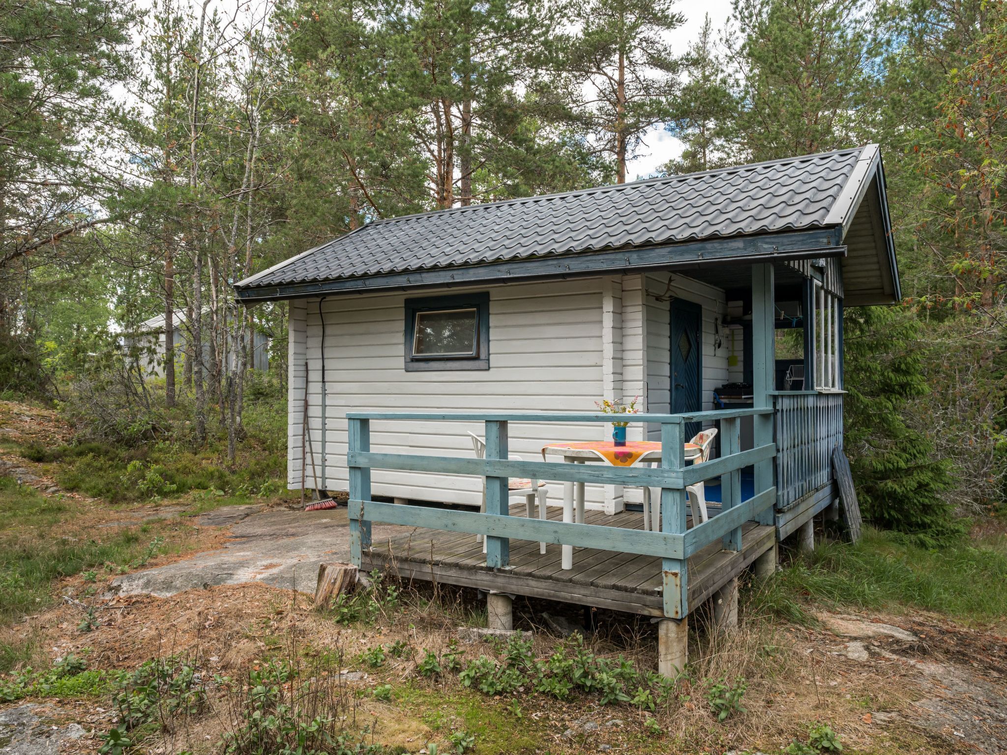 A small cabin with a porch and a table, surrounded by trees.