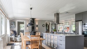 Et moderne køkken med en central ø, indbyggede skabe og et spiseområde med træmøbler.