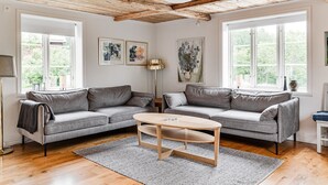 A living room with a wooden ceiling, two grey sofas, a round wooden coffee table, and large windows with a view of greenery. - Klinten Totebo by Interhome (Totebo)