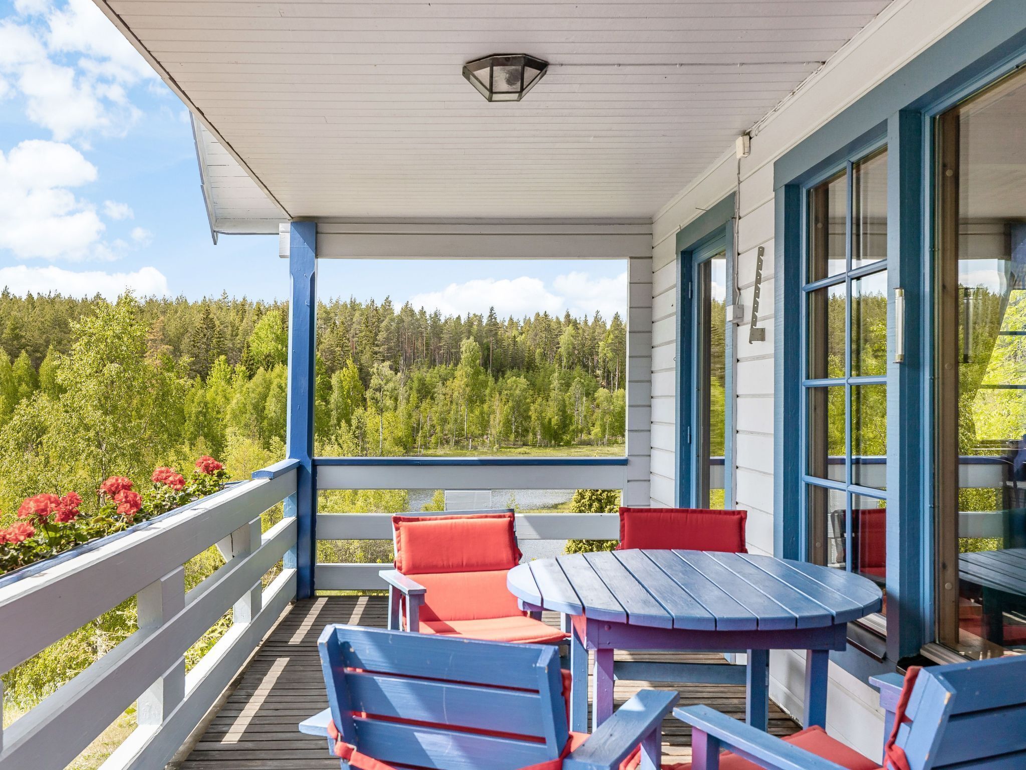 A covered outdoor area with a wooden deck, blue and red furniture, and a view of a forested landscape.