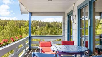 A covered outdoor area with a wooden deck, blue and red furniture, and a view of a forested landscape.