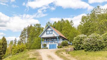 A two-story house with a blue exterior and a white roof, surrounded by greenery and trees.