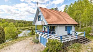 A small house with a red roof, blue trim, and a porch with outdoor seating.
