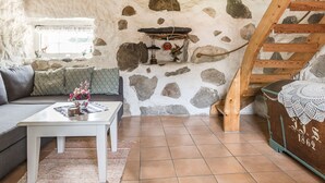 A rustic interior with a stone wall, wooden staircase, and a sofa with a table.