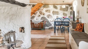 A rustic interior with a stone wall, wooden ceiling, and a cozy seating area with a sofa and chairs.