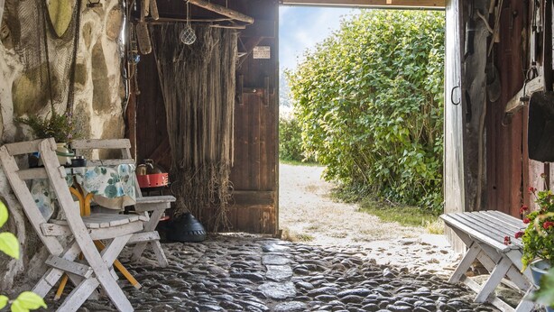 A rustic wooden building with a cobblestone floor, a bench, and a table with a floral tablecloth.