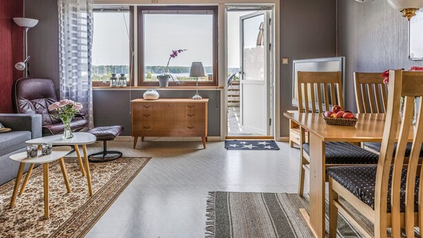 Ein modernes Wohnzimmer mit Holzboden, einem Essbereich mit Tisch und Stühlen, einer Couch, einem kleinen Couchtisch und einem Ausblick durch ein großes Fenster.