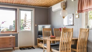 Ein gemütliches Zimmer mit Holzboden, einem Fernseher, einem Esstisch mit Stühlen und einem Fenster mit Blick ins Freie.