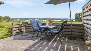 Eine Terrasse im Freien mit Tisch, Stühlen, einem Grill und Blick auf ein Gewässer.
