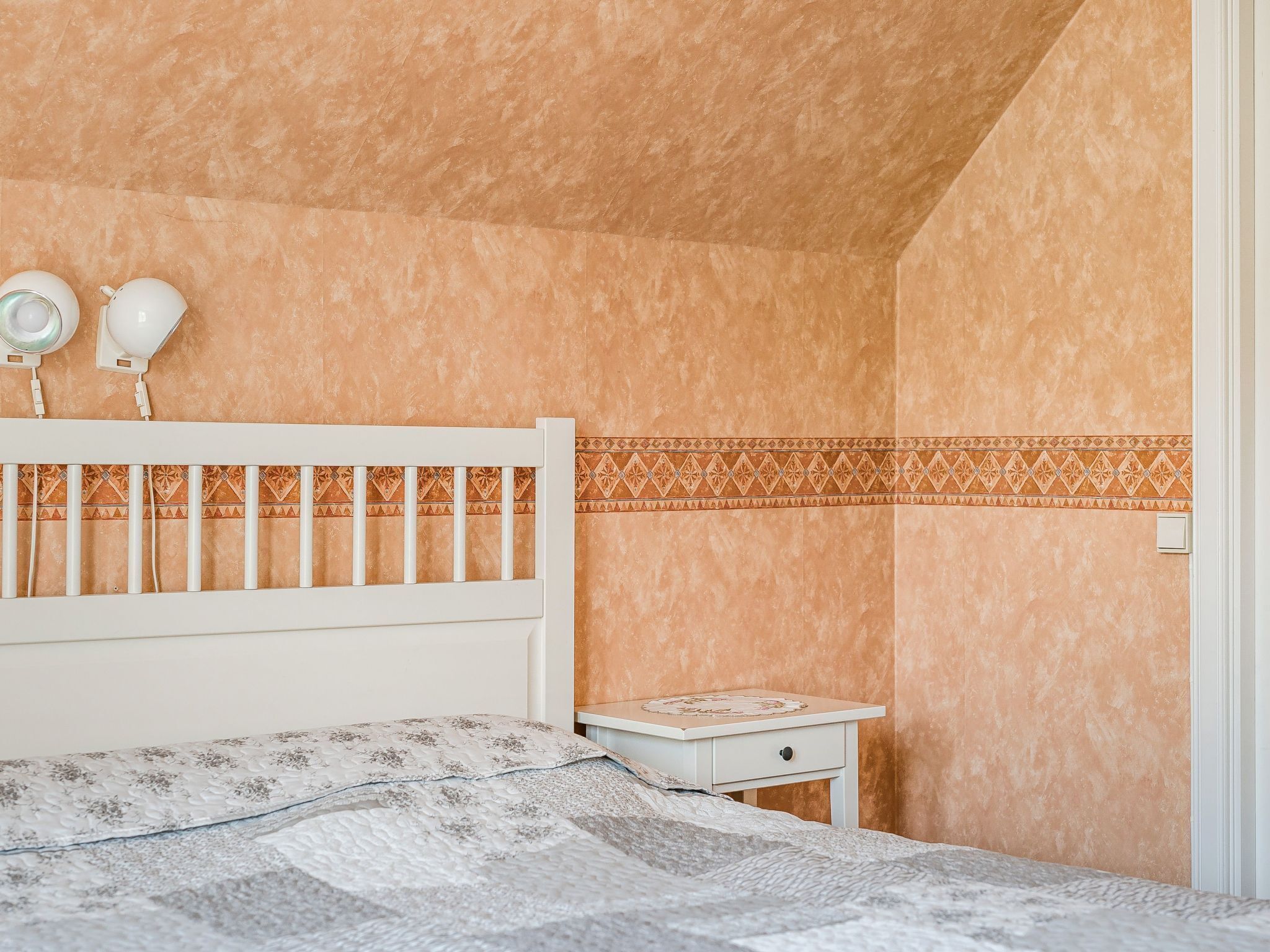 Un dormitorio con cama, mesita de noche, lámpara de pared y cabecero estampado.