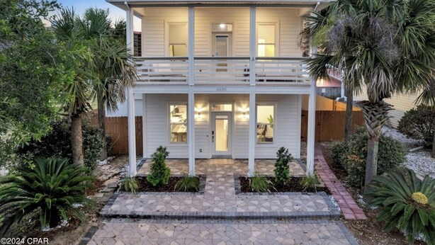 A two-story house with a balcony, surrounded by tropical plants and a paved driveway.