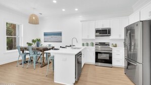 A modern kitchen with white cabinetry, stainless steel appliances, and a wooden dining table with chairs.