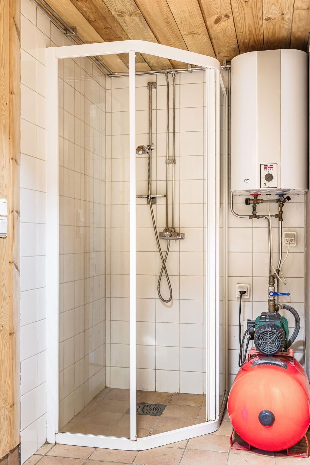 A shower enclosure with a white tiled interior, a visible water heater, and a red pump.