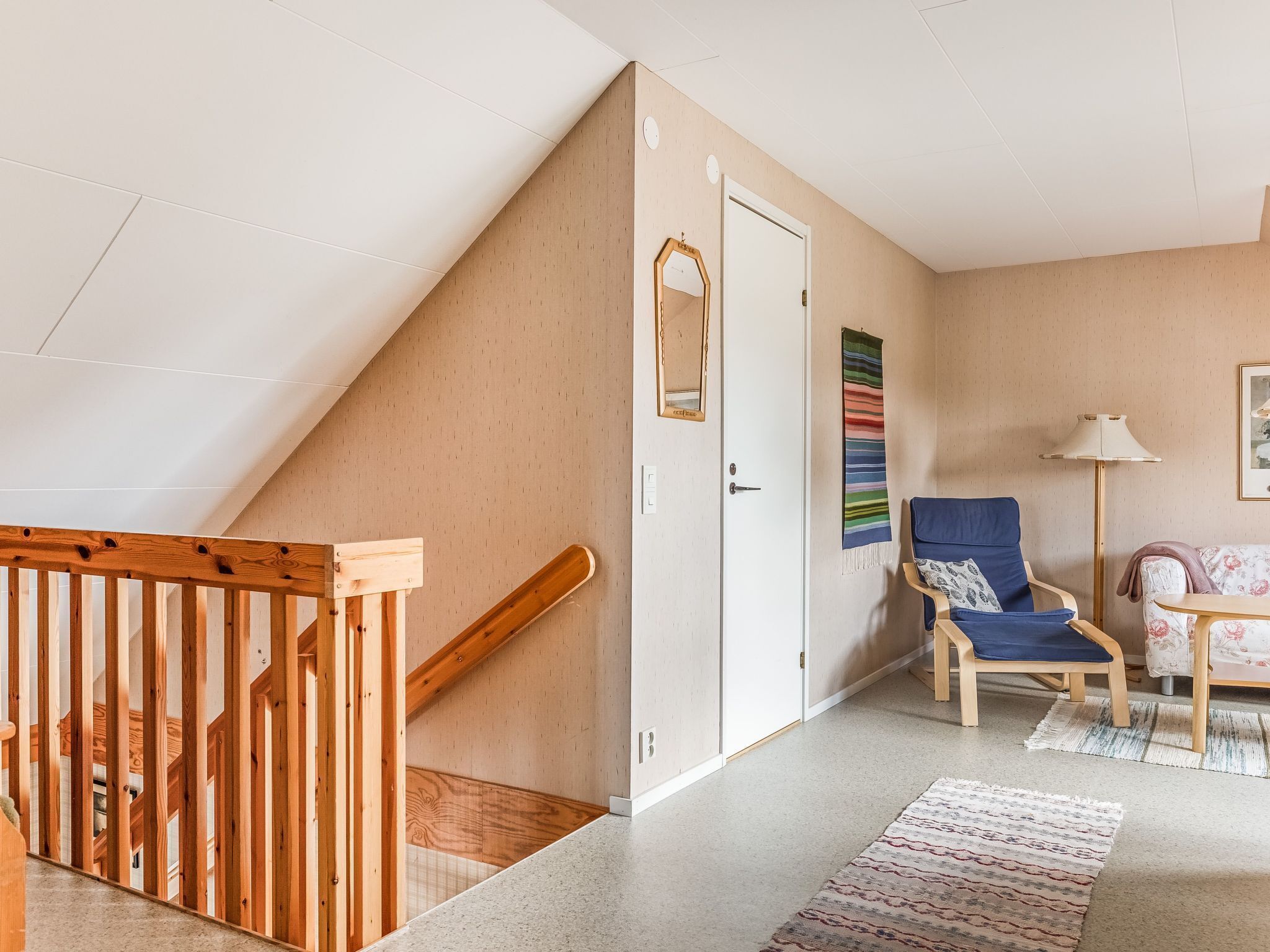 A modern interior with a wooden staircase, a blue chair, a patterned rug, and a lamp.