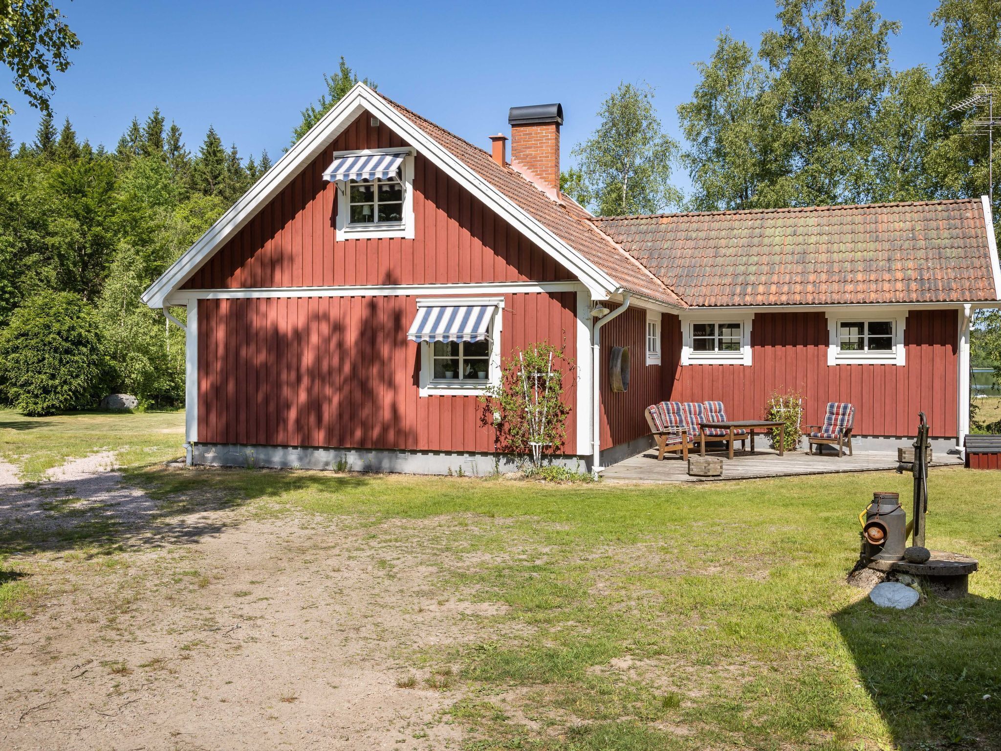 Une maison en bois rouge avec un toit en tuiles, une véranda meublée et un foyer extérieur.