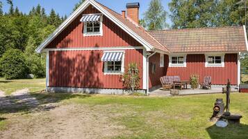 Une maison en bois rouge avec un toit en tuiles, une véranda meublée et un foyer extérieur.