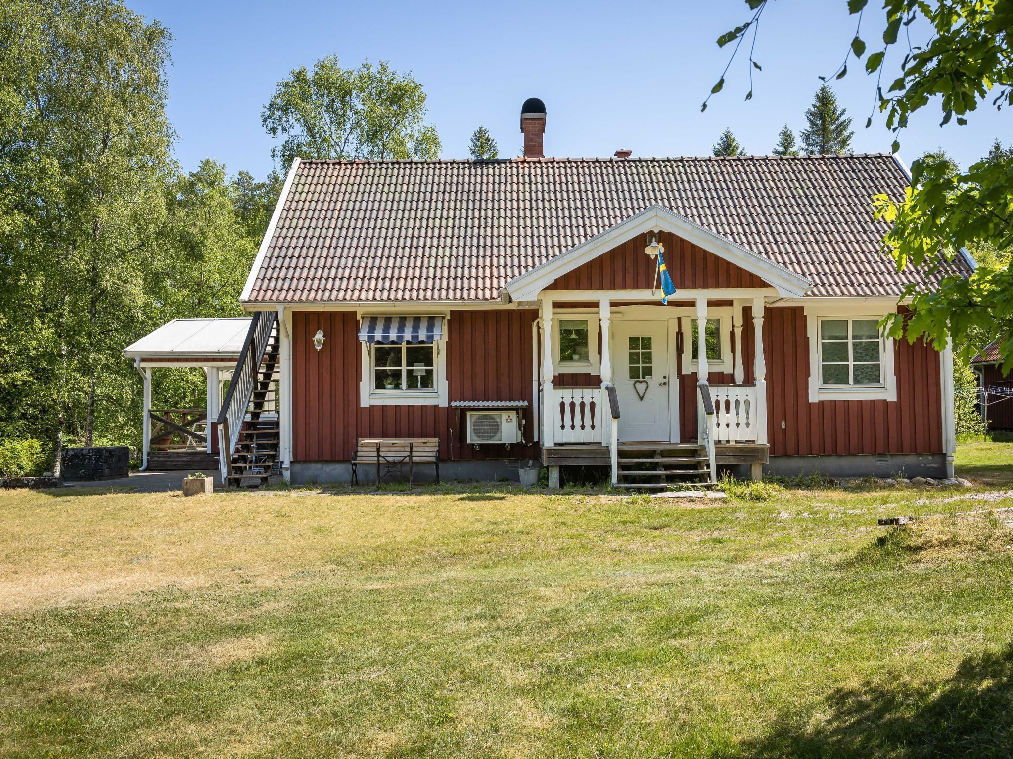 A red wooden house with a white porch, a small attached structure, and a flag.