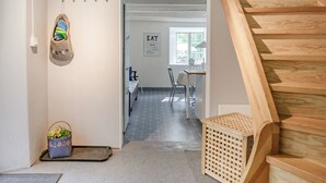 Moderni sisustus, jossa on puinen portaikko, käytävän kautta kuljettava oleskelutila ja seinälle kiinnitetty kenkäteline.